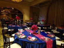 Formal dining room with blue tablecloths, pink runners, and black chairs.