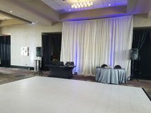Empty event space with a white dance floor, DJ setup, stage backdrop, and speakers.