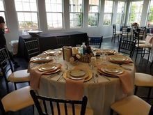 Round table set for a formal event with plates, glasses, and floral centerpiece, in a bright room with windows.