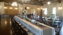 Wedding reception hall with long table, round tables, and stage. Neutral colors, wooden walls.
