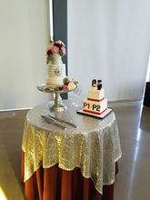 Two-tiered wedding cakes on a round table covered in a silver sequin cloth, with a burgundy skirt.