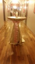 A gold and pink draped cocktail table with a candle sits on a wooden floor in a hallway.