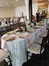 A wedding reception hall with tables set for guests. A person stands near a table decorated with pink and gold.