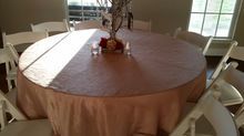 Round table set for event, covered in peach tablecloth. White chairs surround. Centerpiece with crystals and red accents.
