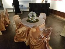 A small round table with gold satin covered chairs, a floral centerpiece, and a buffet table in the background.