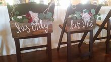 Two wooden chairs with floral arrangements and signs that read 