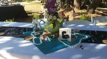 Table setting with a green teapot centerpiece filled with flowers, decorated with pearls and teal accents.