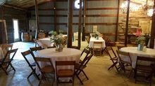 Wedding reception in a barn with round tables, chairs, and floral centerpieces.