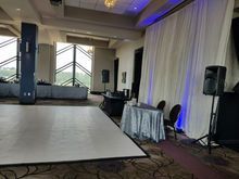 Empty ballroom with dance floor, tables, speakers, and draped backdrop.