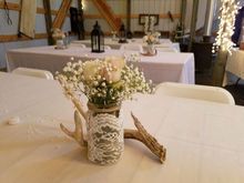 Centerpiece with flowers in a lace-covered jar, antlers, and white tablecloth on a table at an event.