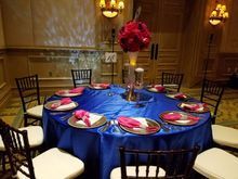 Round table set for a formal event with blue tablecloth, floral centerpiece, and place settings.