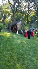 Wedding ceremony with bride in white dress, bridesmaids in red, and guests near an old mill.