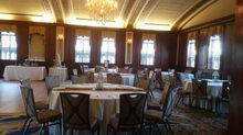 Formal dining room with tables set for a banquet. Wooden walls, windows, and chandelier.