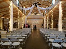 Wedding venue with rows of chairs, draped fabric, string lights, and archway at the end.