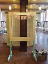 Wooden photo booth frame with a banner and props, set in a reception hall.