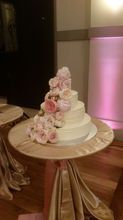 Wedding cake with cascading pink flowers on a draped table, set against a pink-lit wall.