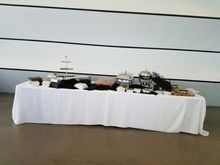 A buffet table with a white tablecloth, various dishes, and serving utensils set against a white wall.