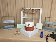 Wedding cake on a table with rustic decor: window, Mr & Mrs banner, trays, and camera.
