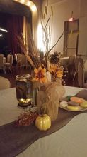 Fall-themed table setting: orange flowers, pumpkin, cookies, and tall grass in a mason jar on a gray table runner.