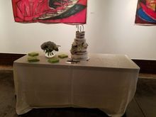 Cake display on a draped table with treats, flowers, and artwork in the background.