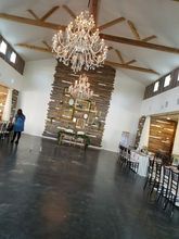Interior of a barn-like venue with chandeliers, wooden wall, and tables set up for an event.