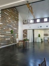 Spacious event venue with wood-paneled wall, dark floor, and high ceiling. A table is set, awaiting a celebration.