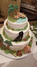 Three-tiered cake with nature scene: trees, lake, couple silhouette, campfire, and tent.