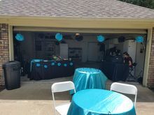Garage decorated for an event with teal and black decor. Tables, chairs, and decorations are set up.