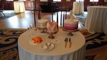 Wedding cakes and desserts on a round table, in a reception hall.