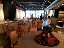 Banquet hall with round tables set for a gathering; tables draped in peach fabric, some people visible in the background.