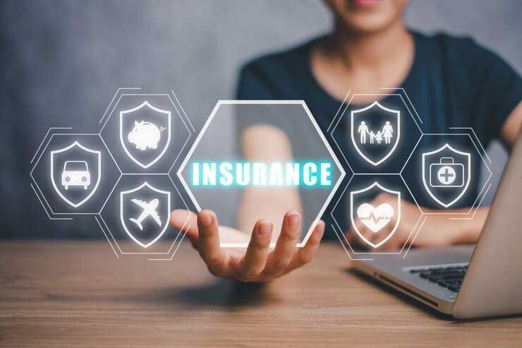 Person at desk presenting glowing “INSURANCE” icons and laptop, with hands reaching toward digital shields