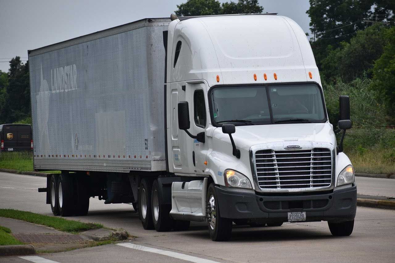 White semi-truck with gray trailer driving on a wet road