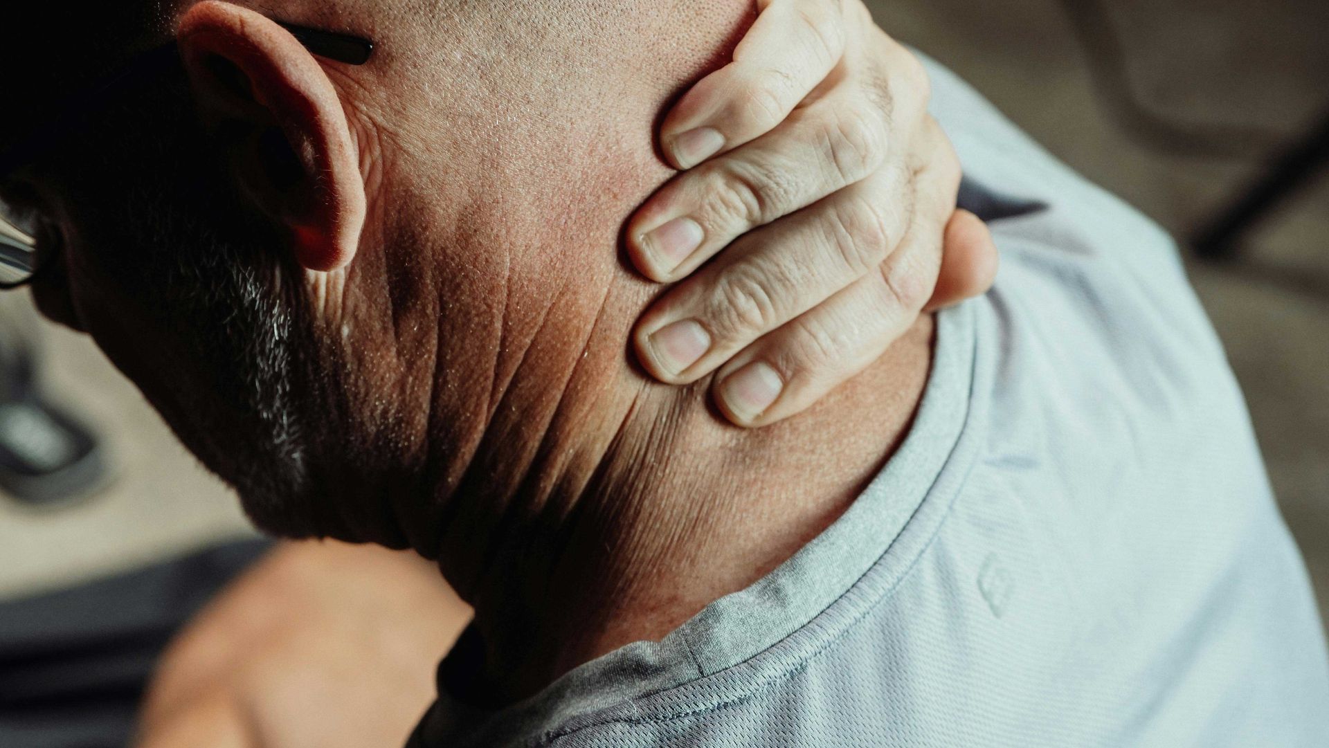 Hand clutching the back of a person’s neck, suggesting neck pain or strain