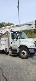 A white truck with a crane on top of it is parked on the side of the road.