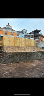 A wooden fence is sitting on top of a dirt hill next to a house.