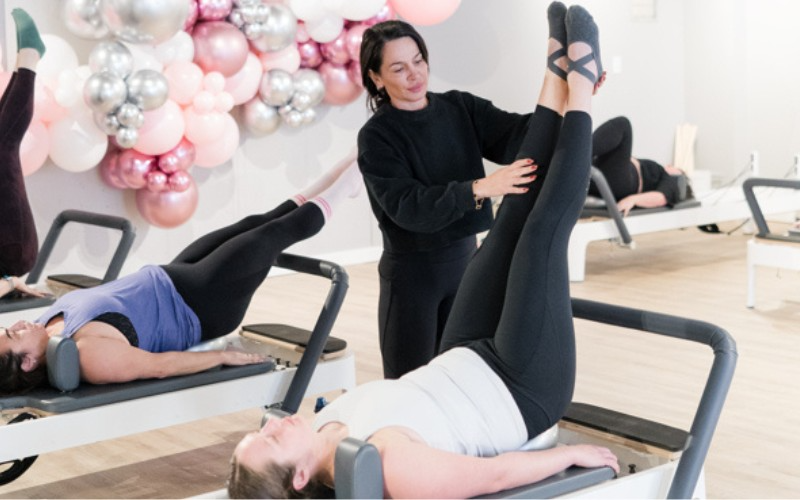 A woman is helping a woman do exercises on a pilates machine.