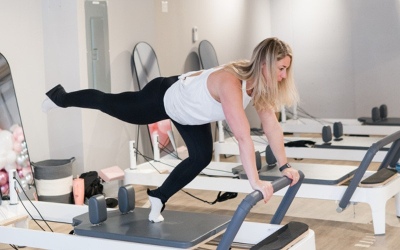 A woman is doing exercises on a pilates machine in a gym.