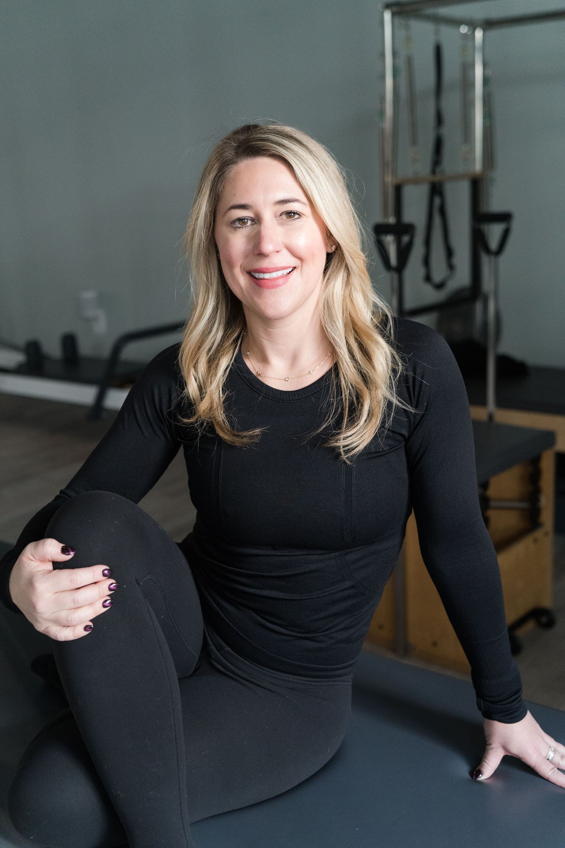 A woman is sitting on a yoga mat in a gym.