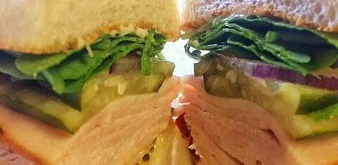 Learn More About Menu Close-up of a sandwich with lettuce, cheese, and sliced meat on bread halves
