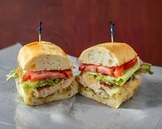 Two stacked sandwiches with tomato, lettuce, and cheese on a gray surface, each held with a toothpick.