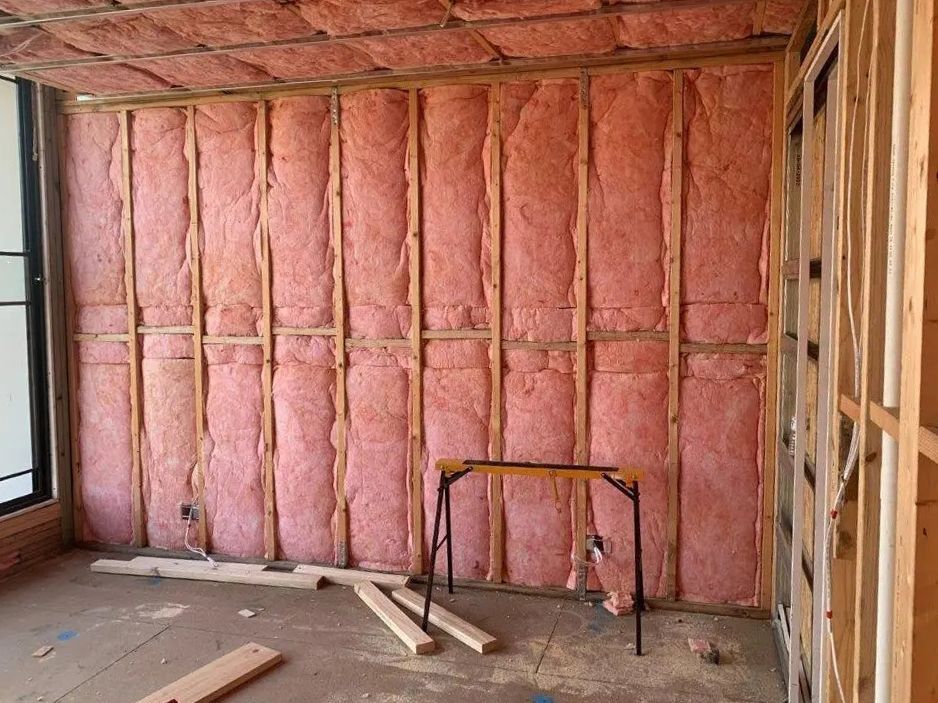 Pink insulation installed between wooden wall studs in a room under construction.