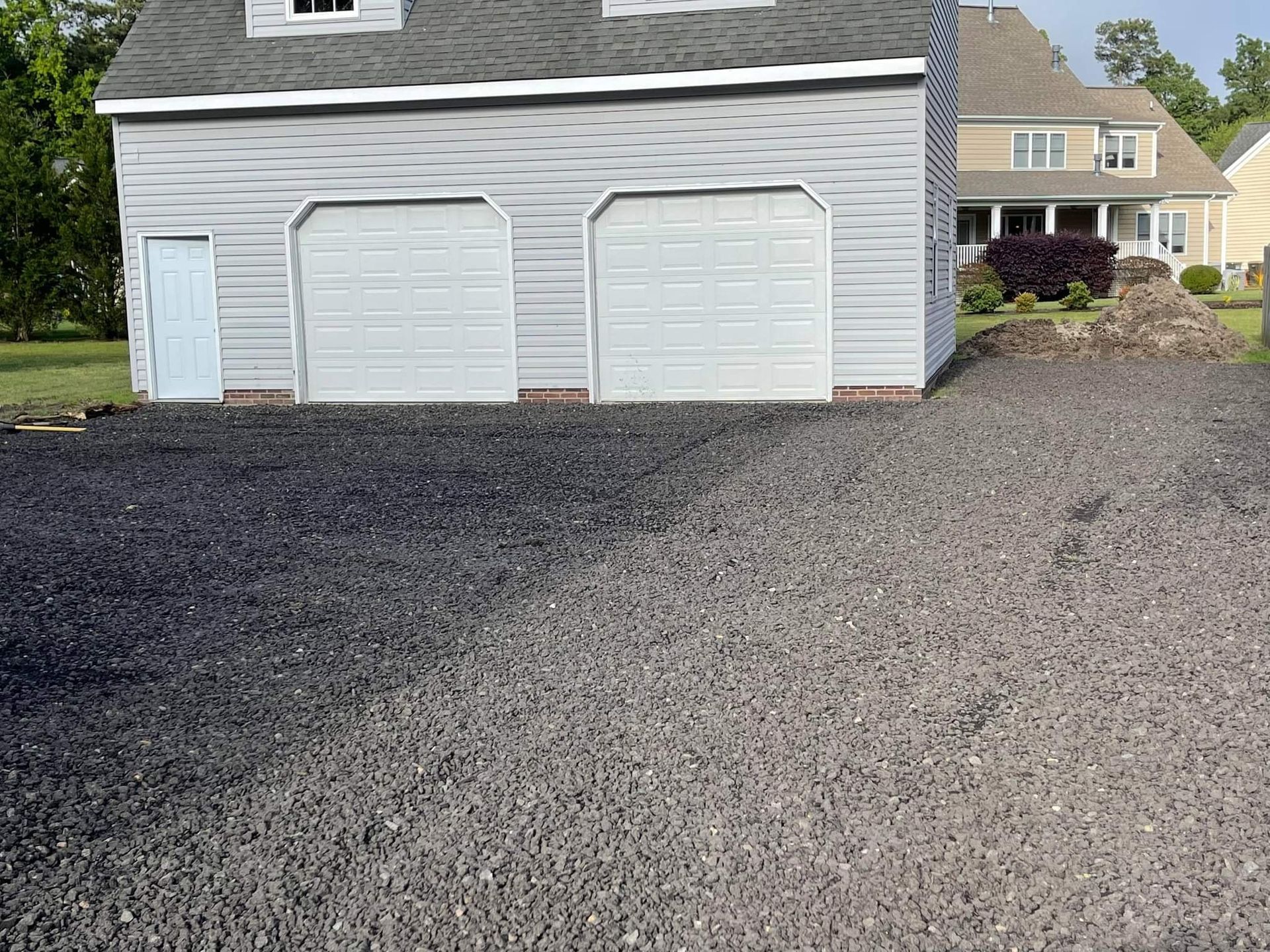 a white garage with two garage doors and a gravel driveway in front of it