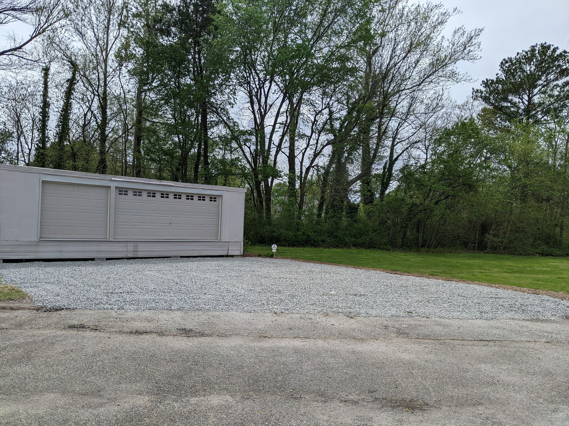 a white garage door is sitting in the middle of a gravel driveway .