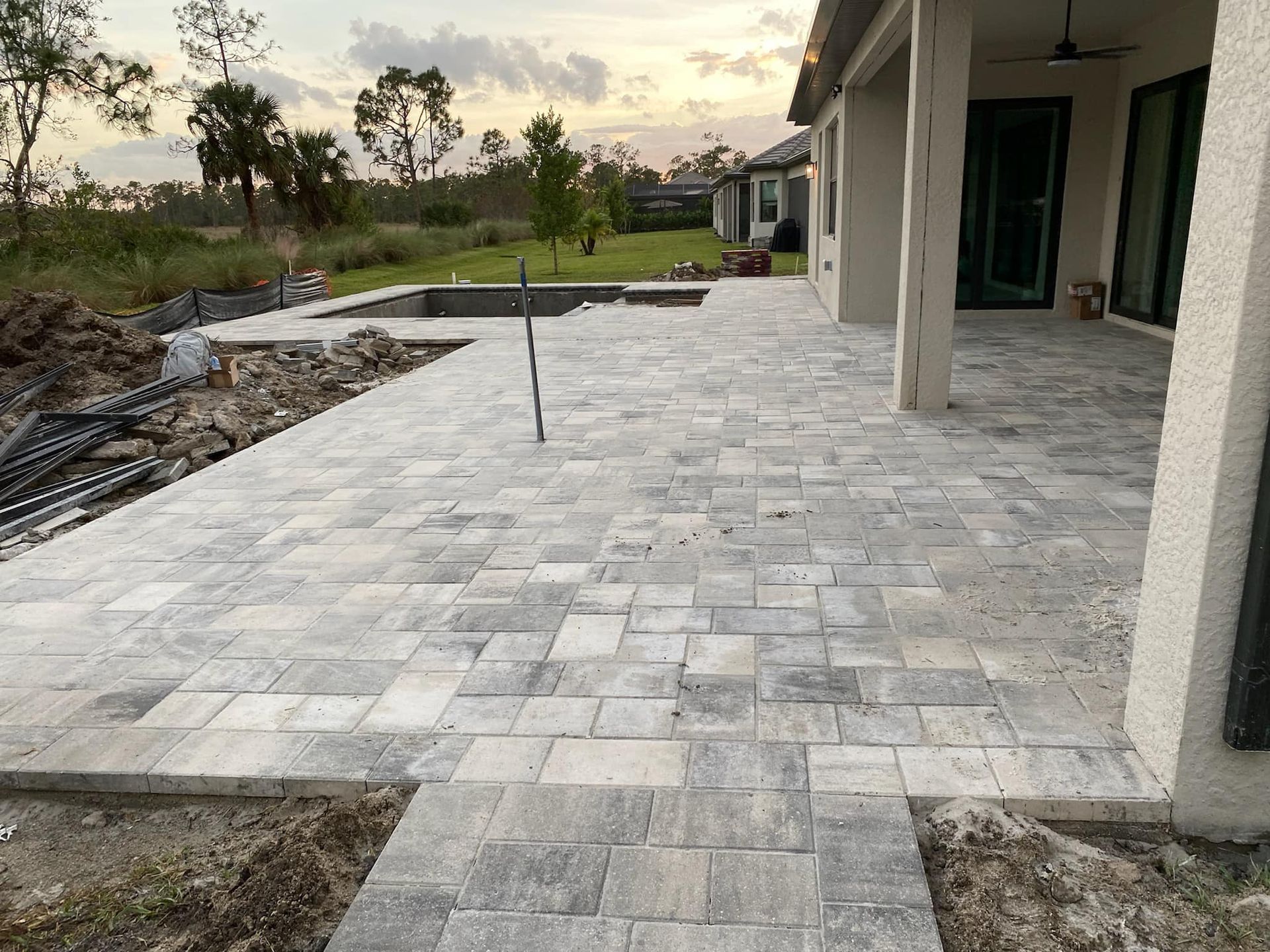 A patio with a pool in the background and a house in the background.