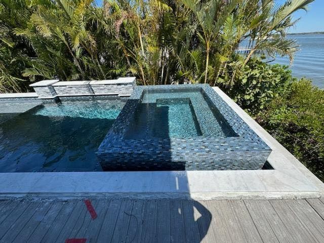 A large swimming pool is surrounded by trees and a wooden deck.