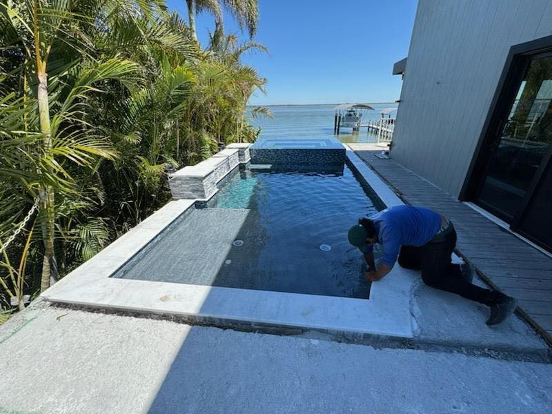A man is working on the side of a swimming pool.