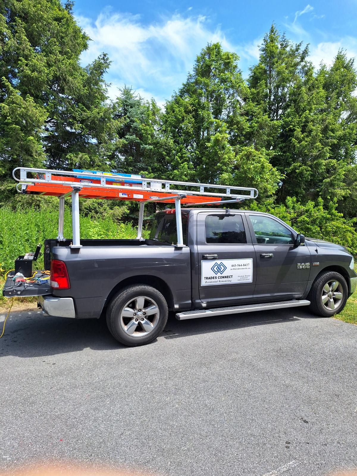 a gray truck with a ladder rack on the back is parked on the side of the road .
