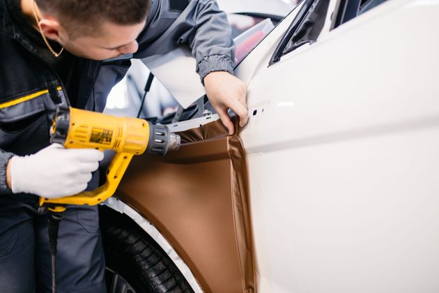 Mechanic using a yellow power drill to work on a car door panel