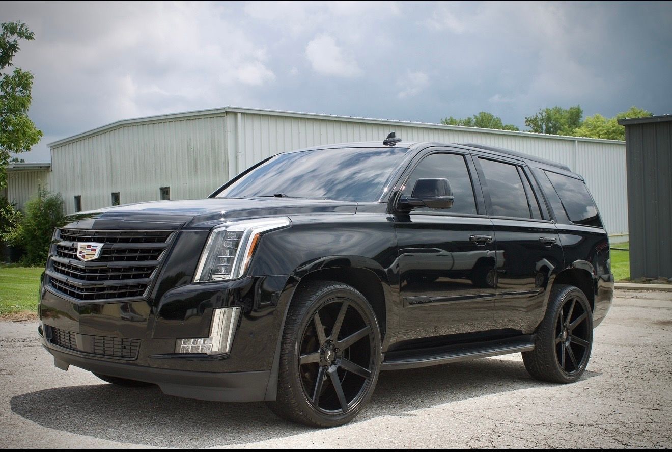 Black Cadillac SUV parked on gravel in front of a metal building under cloudy skies