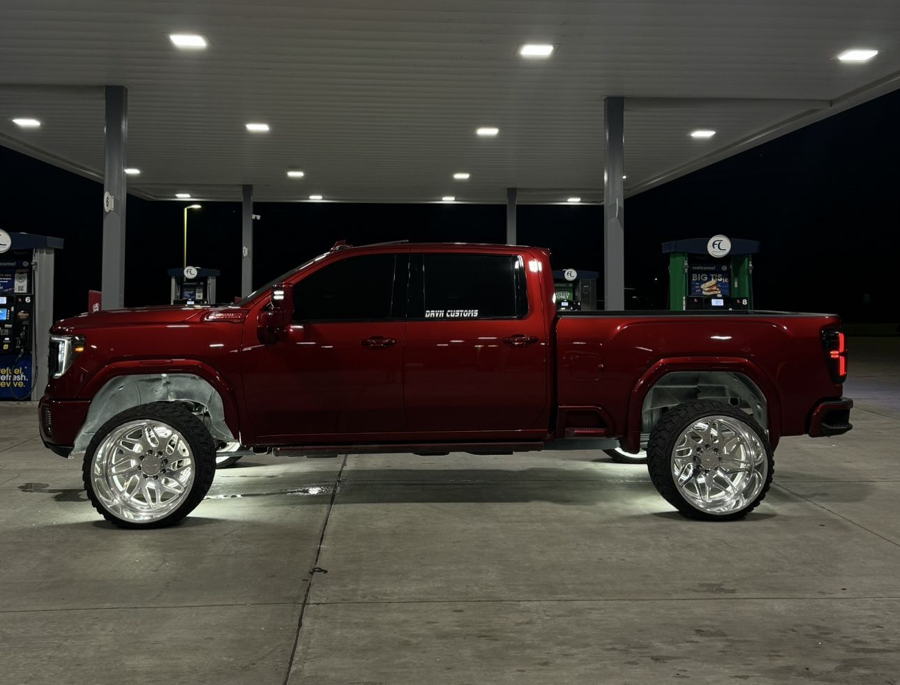 Red lifted pickup truck at a gas station at night, side view